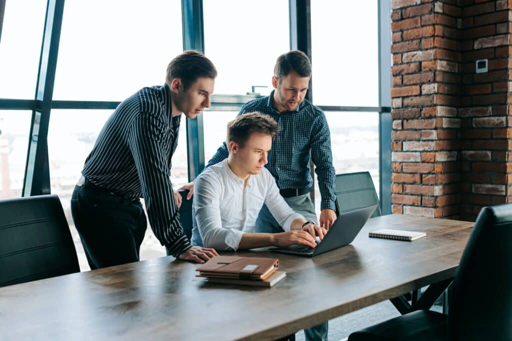 Three men working together on laptops in a modern office space.
