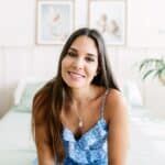 Smiling young adult woman smiling at camera sitting on bed in room