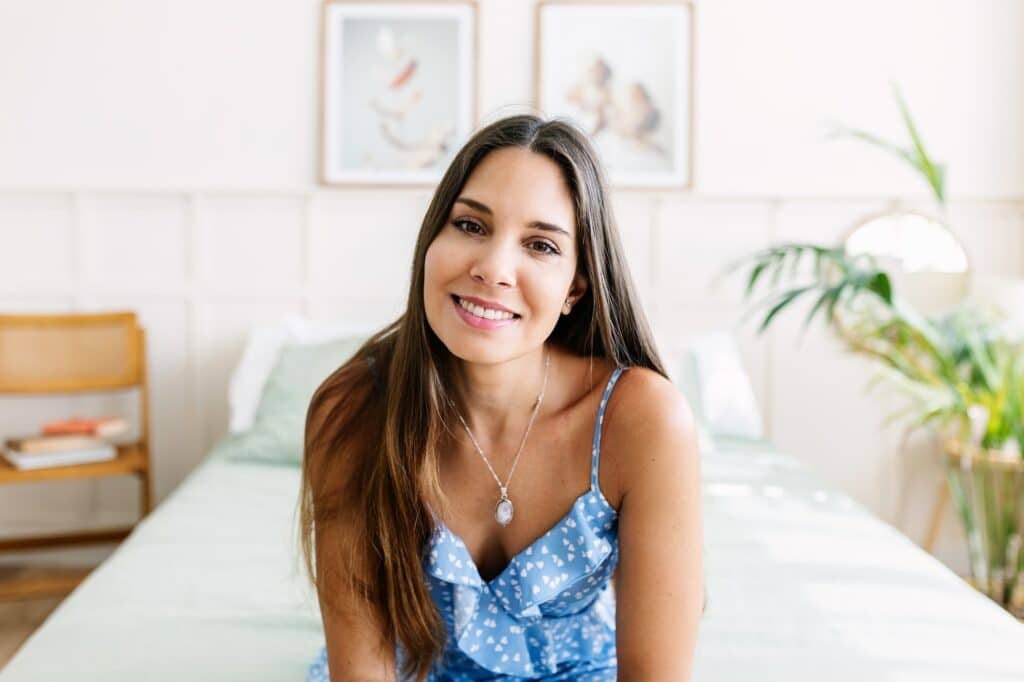 Smiling young adult woman smiling at camera sitting on bed in room