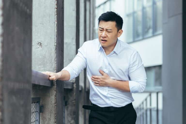 Asian office worker sick, having severe chest pain, businessman holding hands on heart