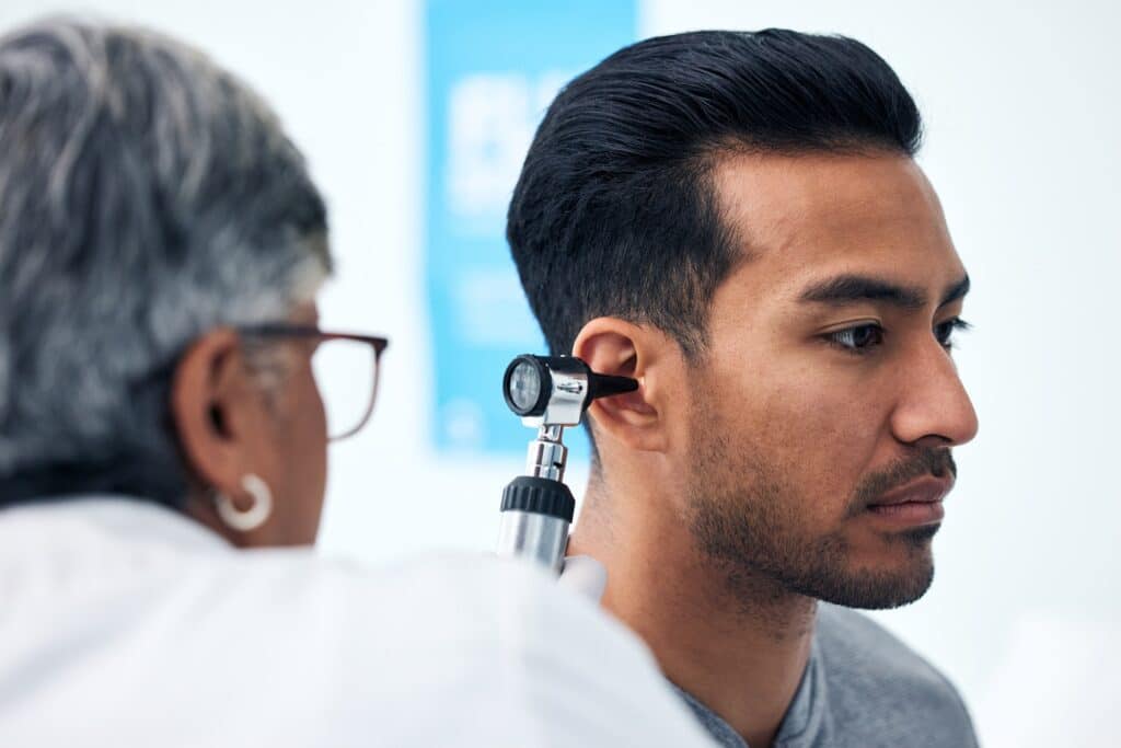 Ear check, man and clinic doctor with patient consultation for hearing and wellness at hospital. Se