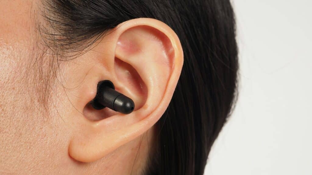 Black earplugs in ear on white background.