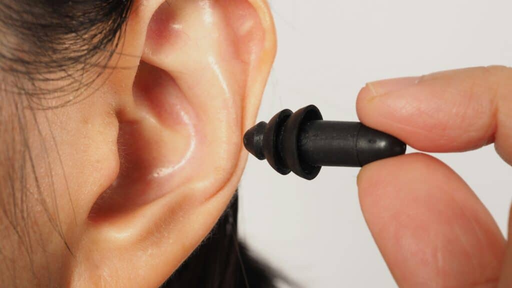 Hand is hold black earplug and ear on white background.